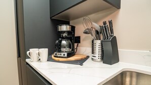 A kitchen with a coffee maker, two white mugs, a knife block, and a sink.