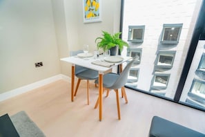 A dining area with a table set for four, a potted plant, and a window with a view of a building. - Modern 1BR Apt near Solihull & Central Birmingham (West Midlands)