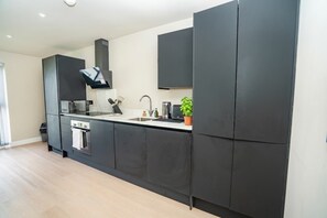 Une cuisine moderne avec des meubles de rangement de couleur sombre, un four encastré, un four à micro-ondes et un évier.