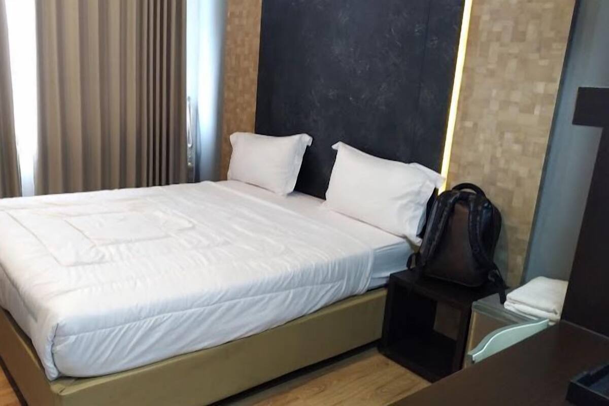 A neatly made bed with white linens in a hotel room.