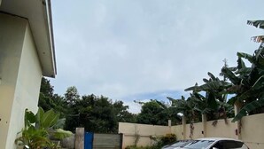 Un'area di parcheggio con una moto e un'auto bianca, circondata dal verde e da un edificio con una porta blu.