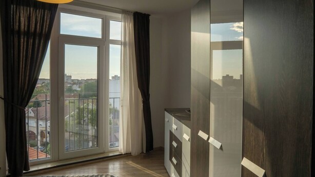 Une chambre avec une grande fenêtre, un lit, une armoire et un bureau.