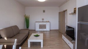 Un salon moderne comprenant un canapé, une table basse, un téléviseur et un coin cuisine avec des placards et un réfrigérateur.