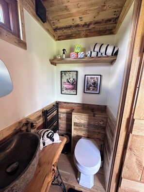 A rustic bathroom with a wooden vanity, a large basin, a toilet, and shelves with toiletries. - Charming Shepherds Hut in peaceful Lydiard Millicent walking distance to pub (Lydiard Millicent)