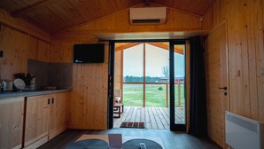L’intérieur d’un chalet en bois comprend un coin cuisine, un téléviseur et une porte-fenêtre coulissante qui donne sur une terrasse.