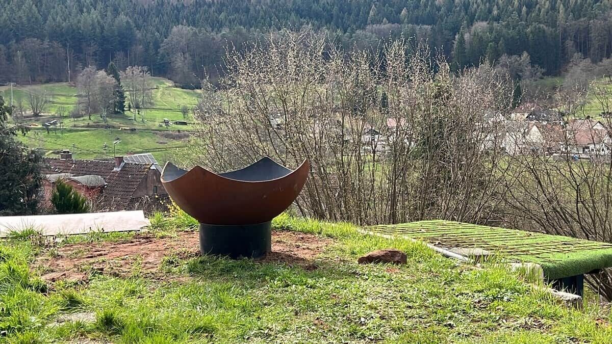 Un paysage avec une grande structure à la forme unique au premier plan, une zone herbeuse et un village en arrière-plan.