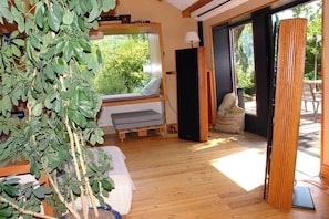 A room with a wooden floor, a window seat with a cushion, a speaker, and a plant.