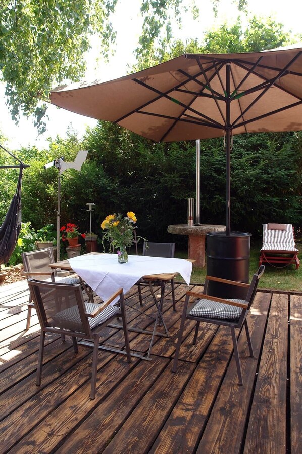 Um pátio externo com mesa e cadeiras, uma cadeira suspensa, churrasqueira e uma fonte decorativa.
