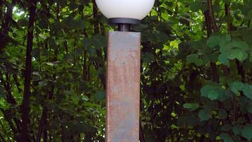 A standalone lamp post with a spherical light fixture, set against a backdrop of dense foliage.