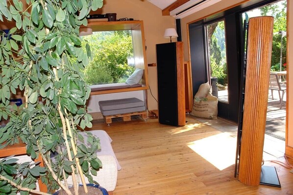 Ein Zimmer mit Holzboden, einer Sitzbank mit Kissen, einem Lautsprecher und einer Pflanze.