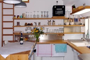 Cozinha com prateleiras de madeira, micro-ondas e mesa de jantar com uma garrafa de vinho e copos.