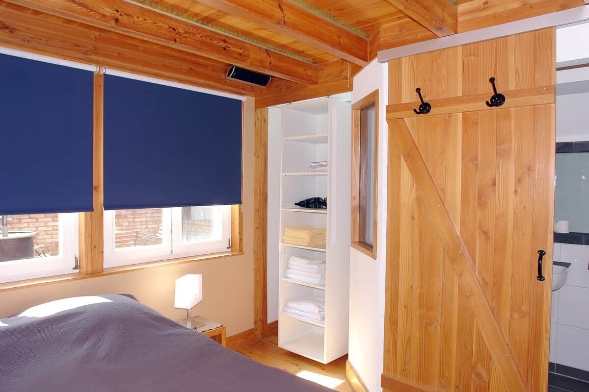 Un dormitorio con cama, ventana con persiana, armario de madera y estantería blanca.
