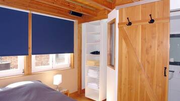 Un dormitorio con cama, ventana con persiana, armario de madera y estantería blanca.