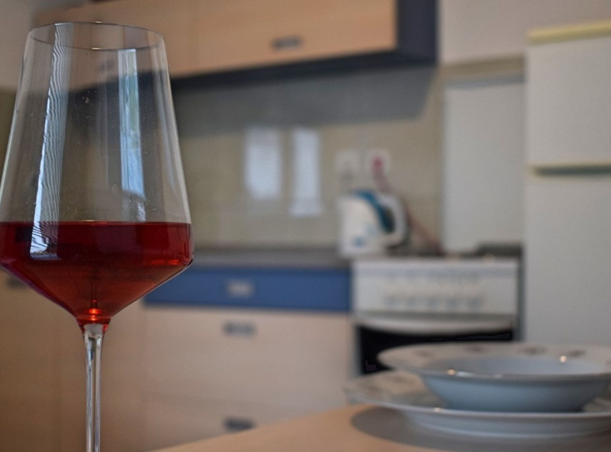 A glass of red wine on a table in a kitchen with cabinets and a microwave.