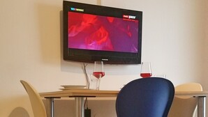 A hotel room with a flat-screen TV mounted on the wall, a wooden table with two chairs, and a wine glass on the table.