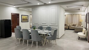 A modern dining area with a round table and six chairs, a black refrigerator, and a beige sofa in the background.