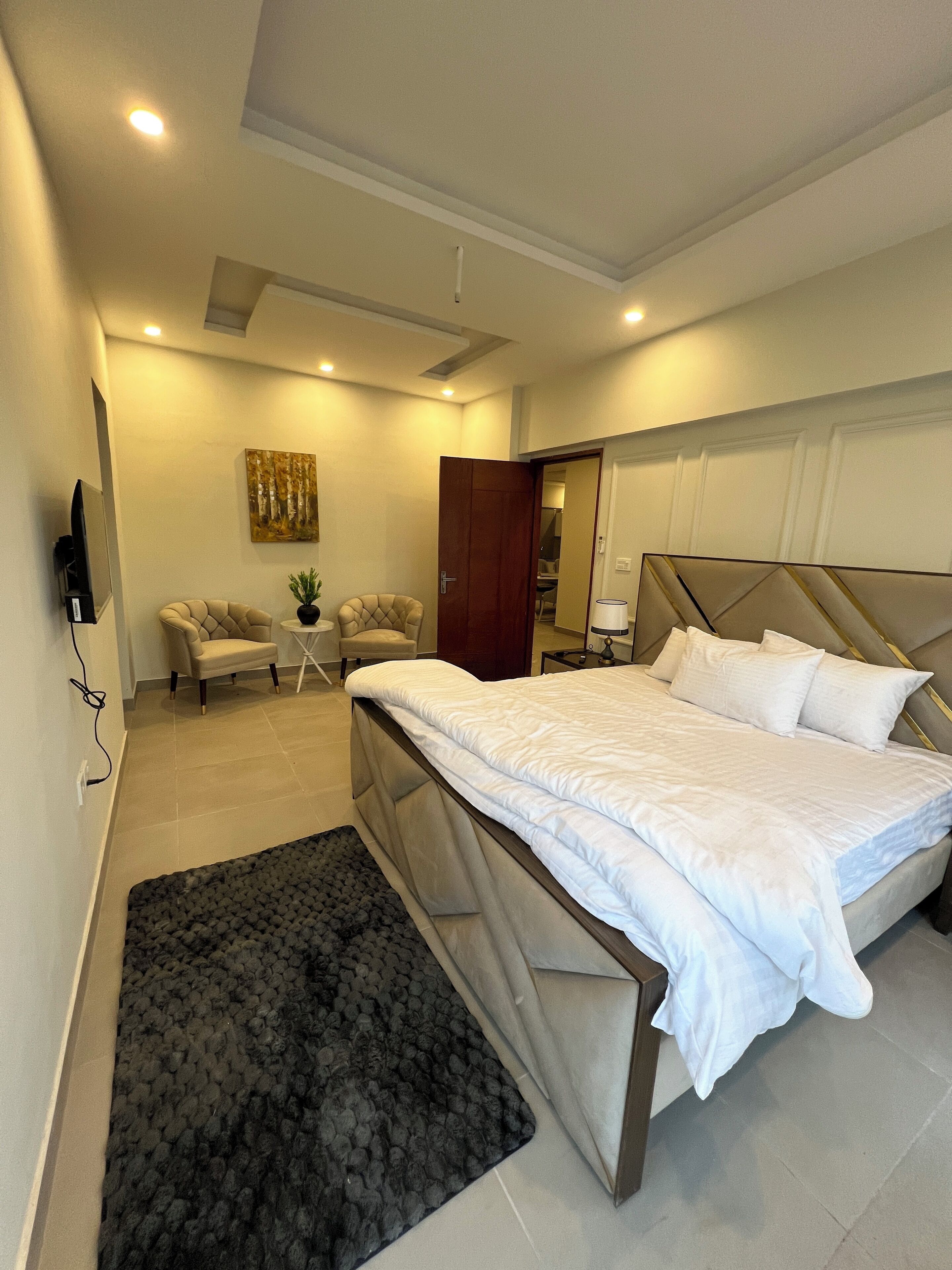 Quarto moderno com uma cama, duas poltronas, uma mesinha e um quadro na parede.