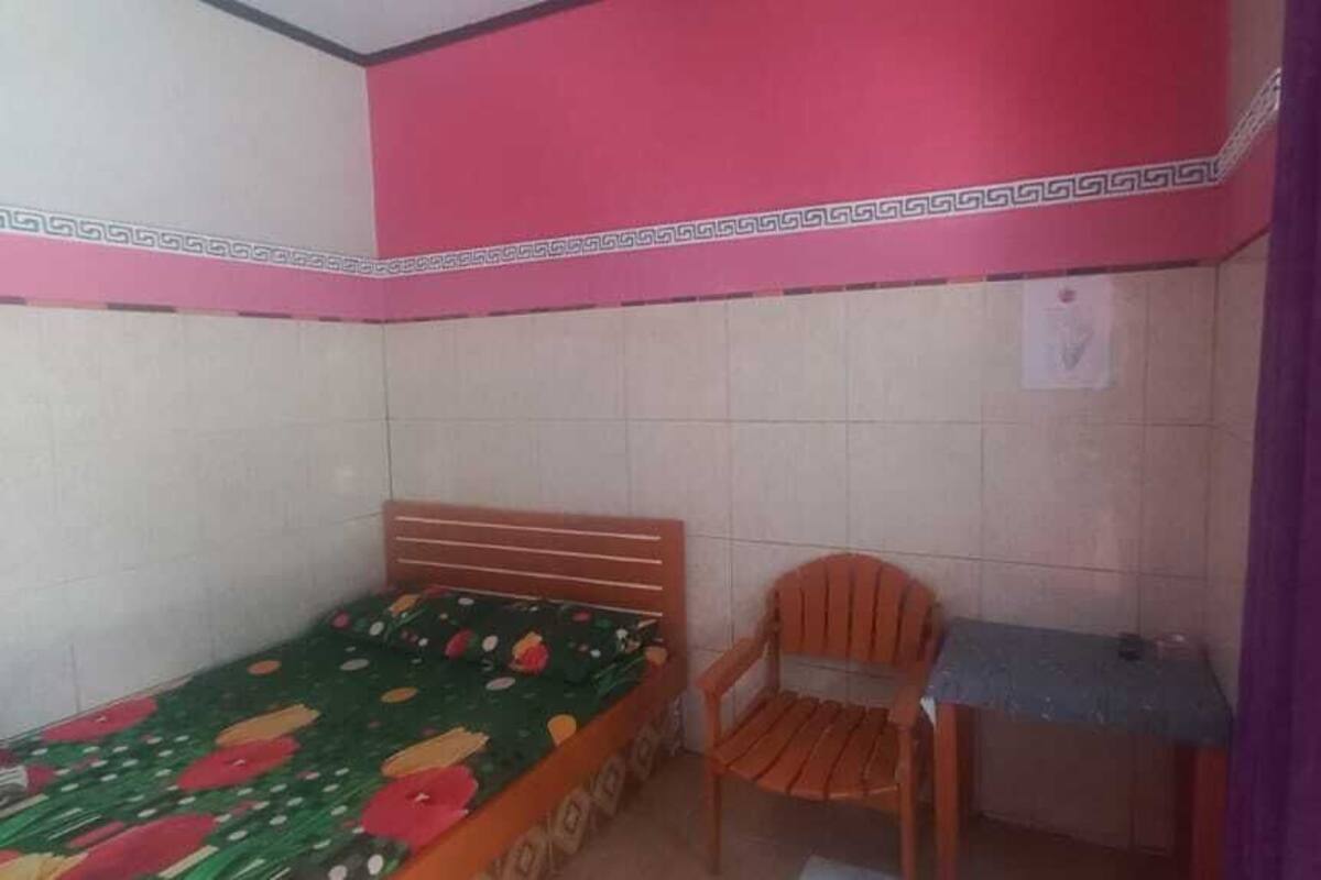 Une petite chambre avec un lit simple, une tête de lit en bois, une chaise et un bureau.