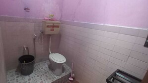 Une petite salle de bain avec des toilettes, un seau et une poubelle.
