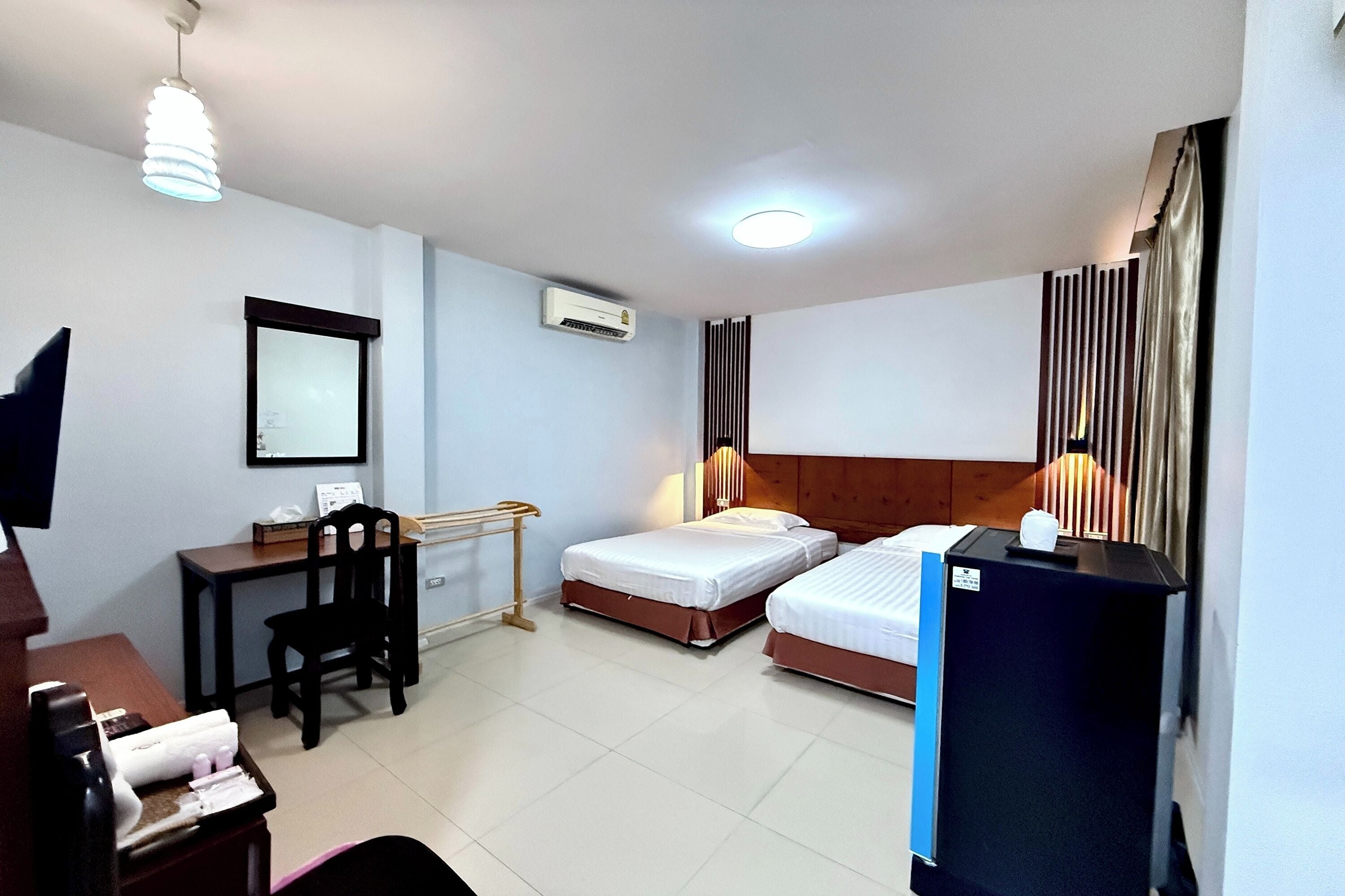 A hotel room with two beds, a desk with a chair, a TV, and a minibar.
