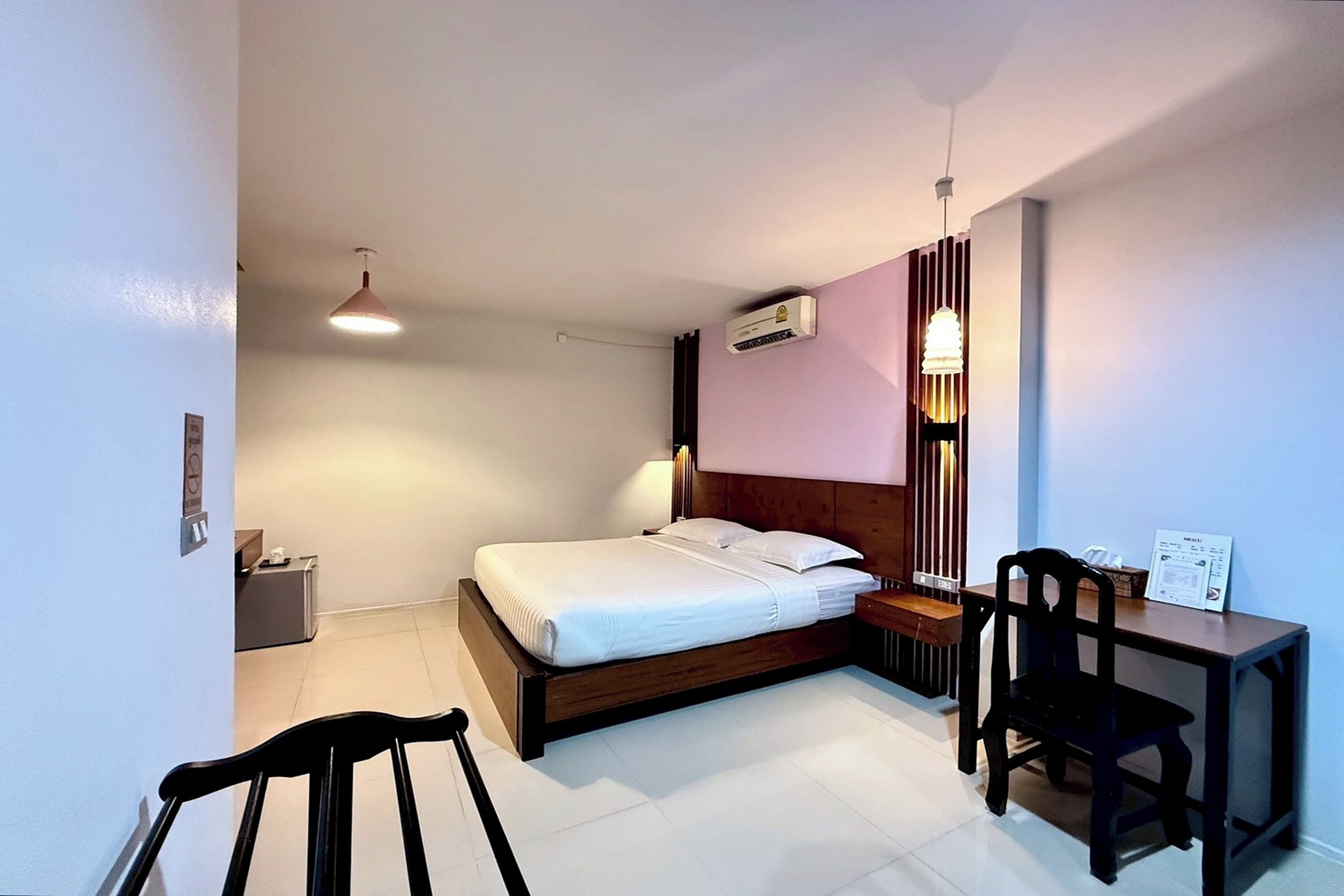 Habitación de hotel con cama, mesita de noche, silla, escritorio y unidad de aire acondicionado.