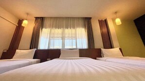 Une chambre d’hôtel avec deux lits, une grande fenêtre avec des rideaux et deux lampes fixées au mur.