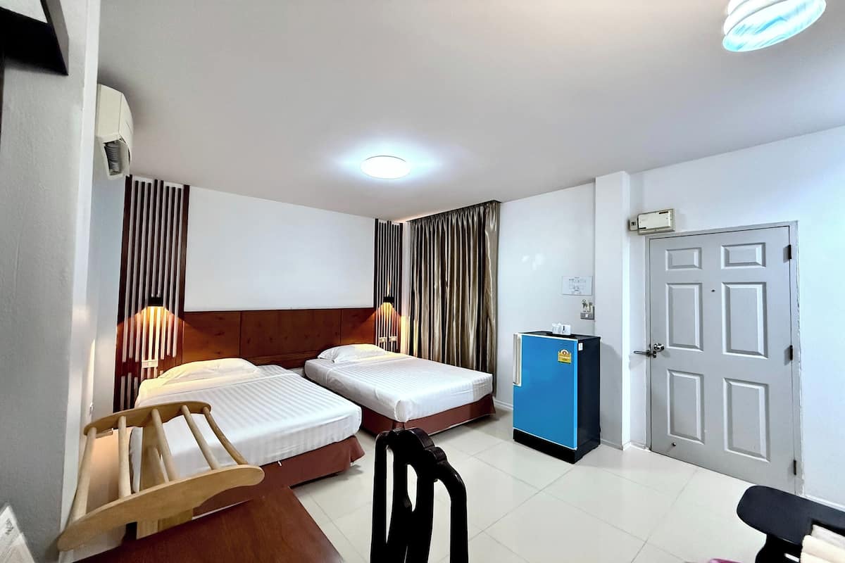 Ein Hotelzimmer mit zwei Betten, einem Schreibtisch, einem Stuhl, einem Kleiderschrank, einer Schreibtischlampe und einer Tür.
