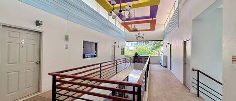 A modern hotel corridor with a staircase, a flat-screen TV, and a balcony with a view.