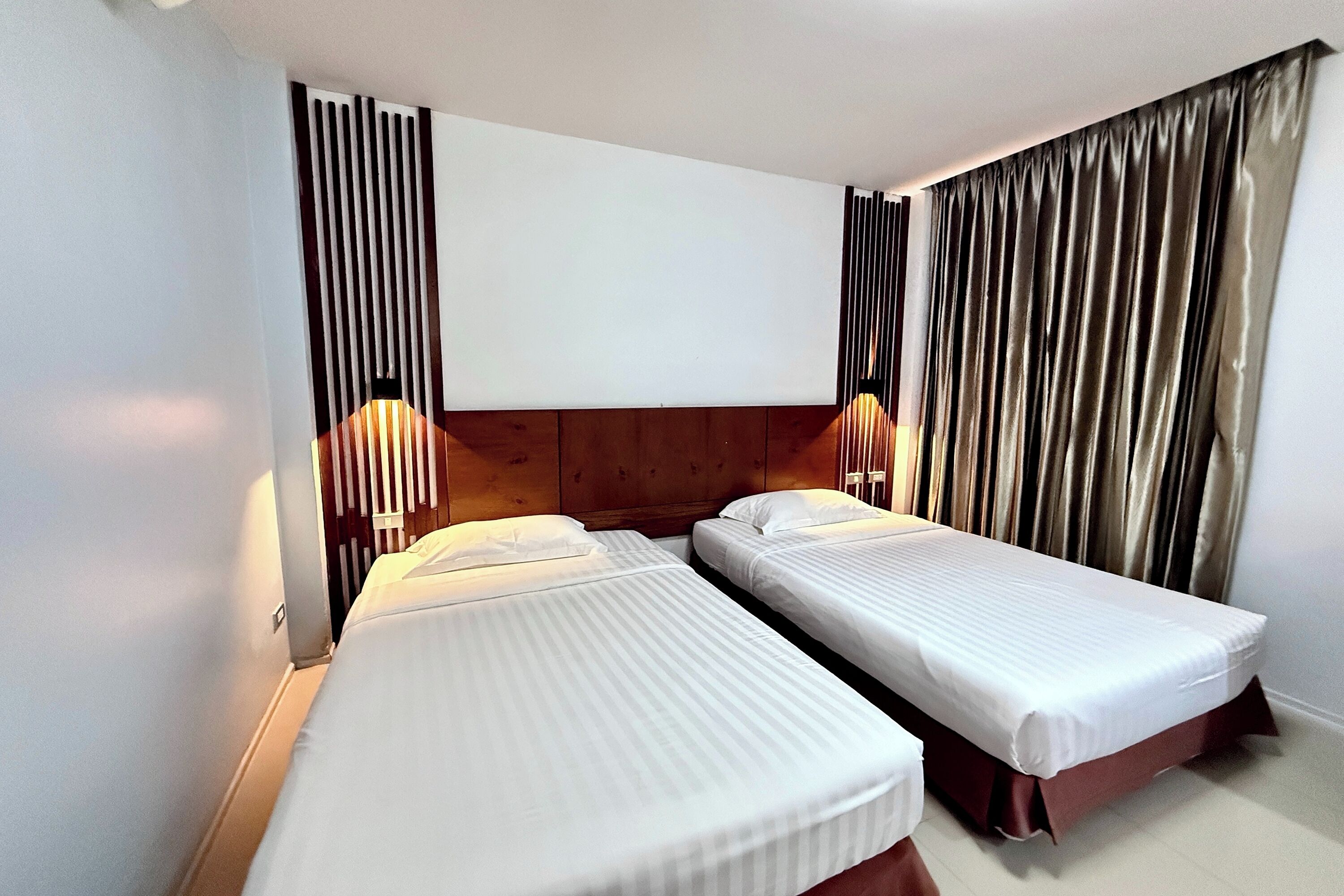 A hotel room with two single beds, a wooden headboard, and a large window with curtains.