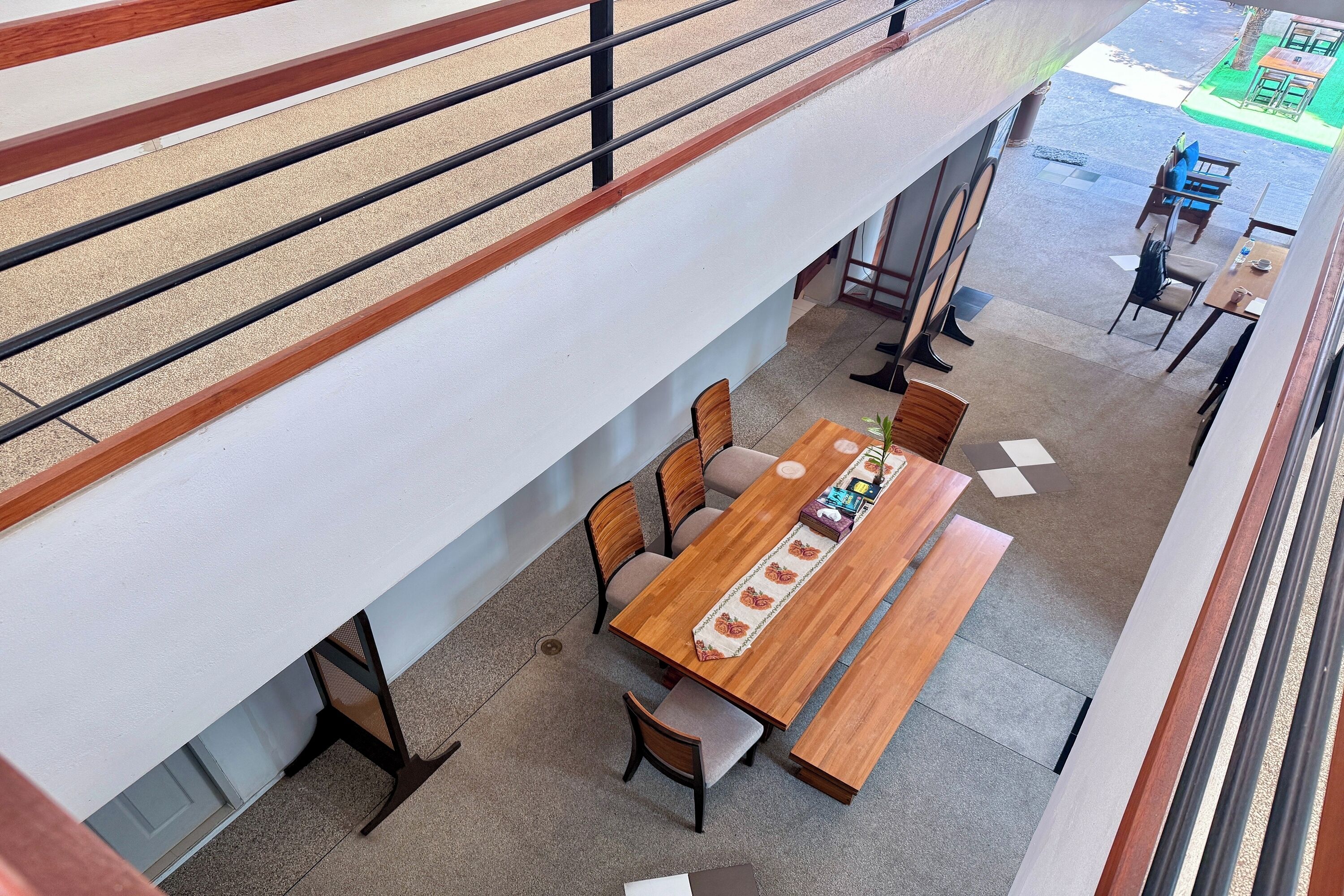 A modern interior with a long wooden table and chairs, a white wall, and a balcony with a railing.