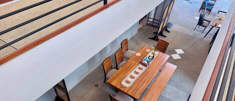 A modern interior with a long wooden table and chairs, a white wall, and a balcony with a railing.