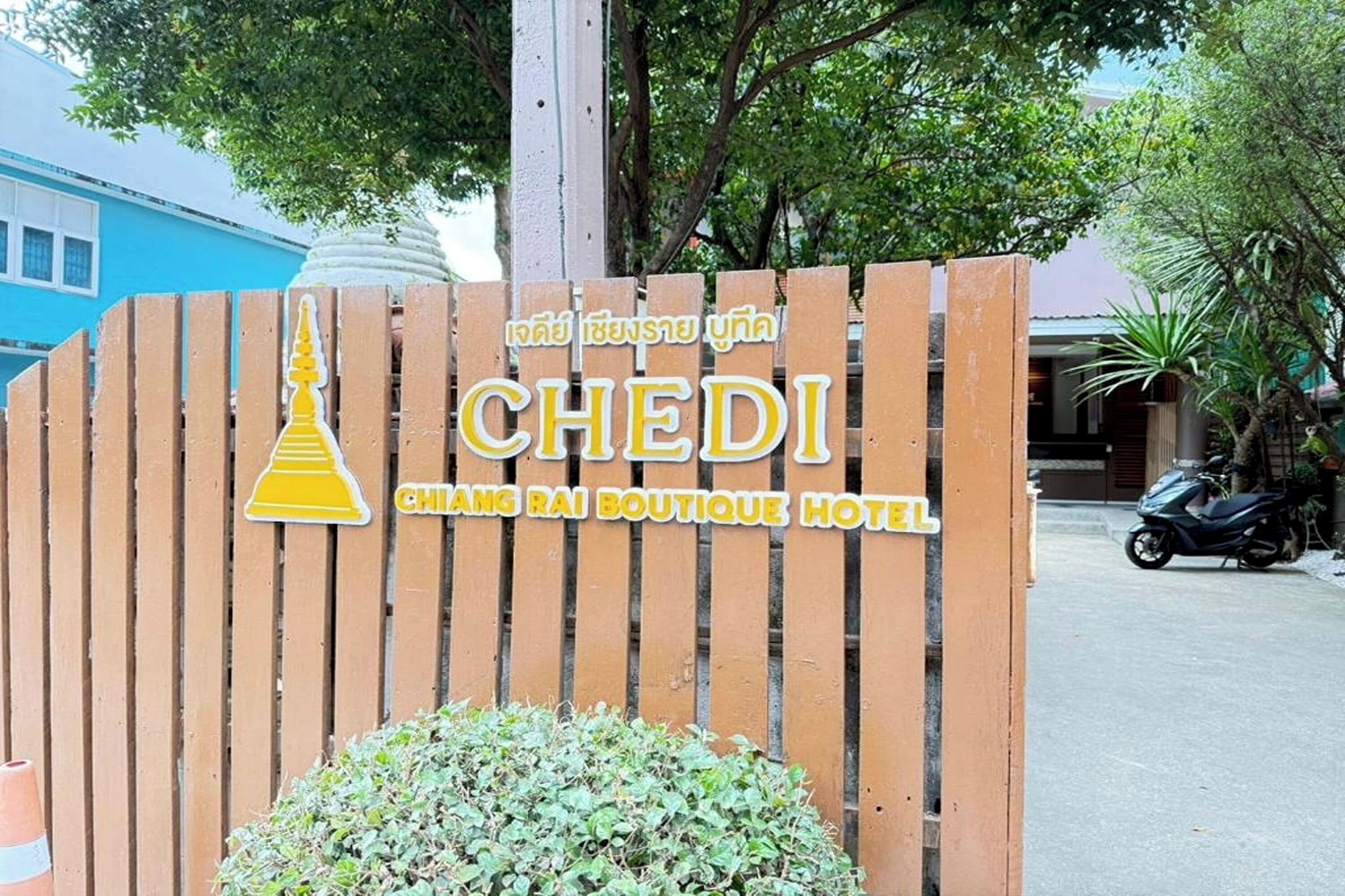 Ein Holzschild mit der Aufschrift 'CHEDI' und 'CHANG RAI BOUTIQUE HOTEL' in Thai und Englisch.