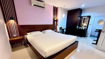 A modern hotel room with a large bed, a wooden headboard, a bedside table, a wardrobe, a mirror, and a bathroom with a sink and toilet.