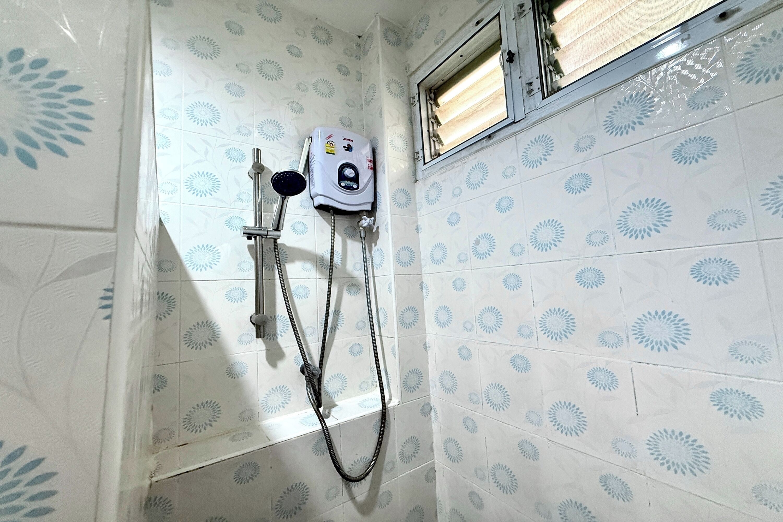 Un baño con ducha, calentador de agua y azulejos estampados.