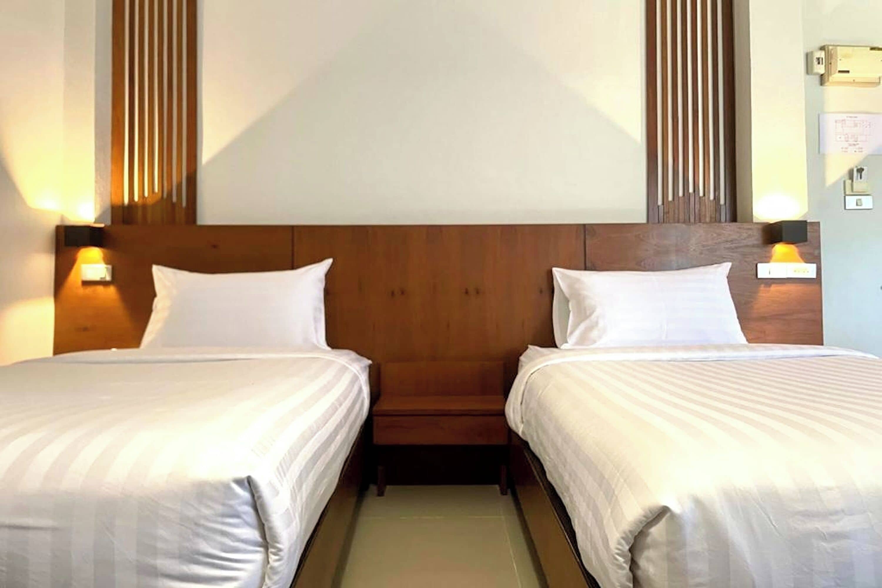 Habitación de hotel con dos camas individuales, cabecero de madera, lámparas de noche y un panel de pared de madera.