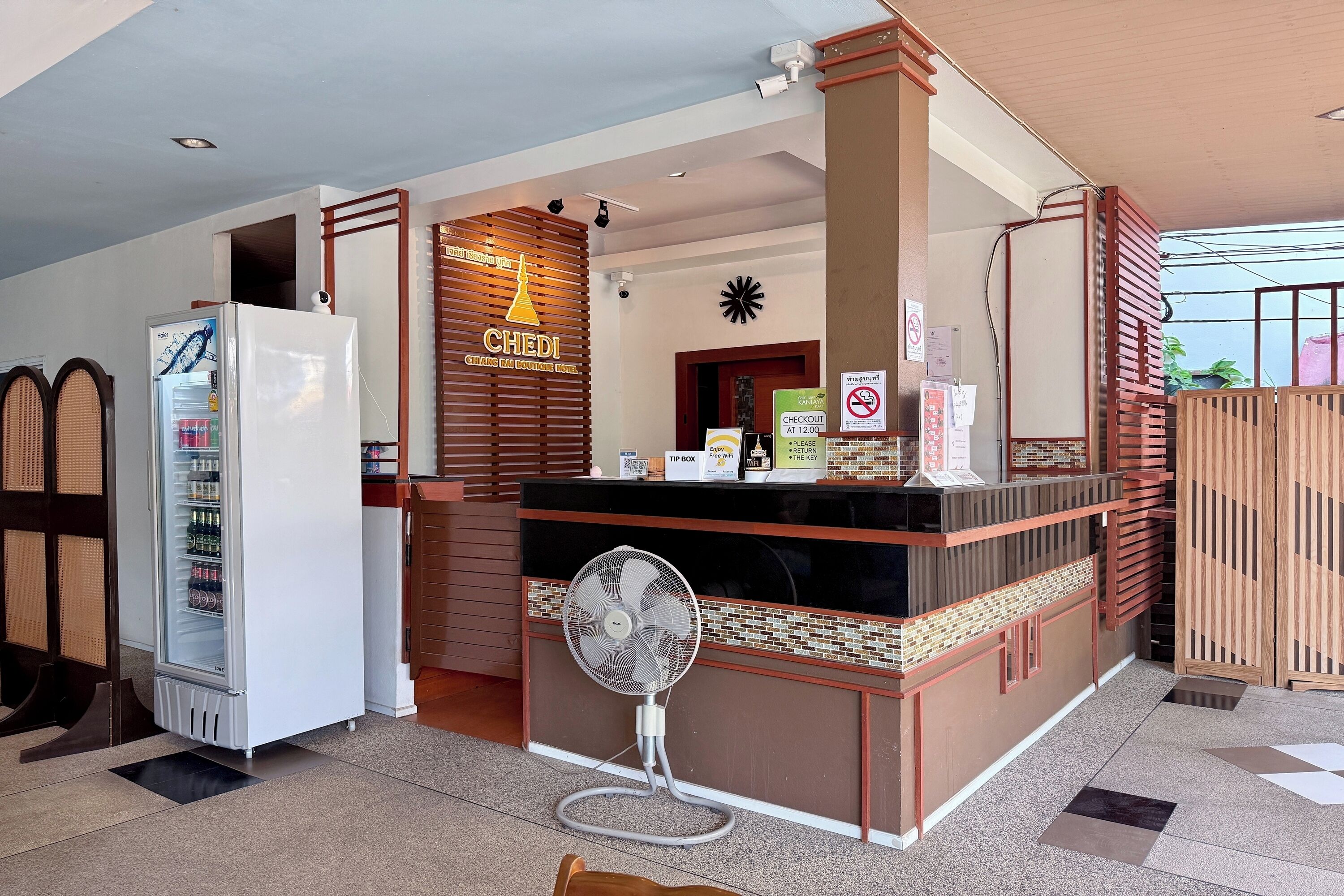 Zona de recepción de un hotel con un refrigerador, un ventilador y una barra de madera.
