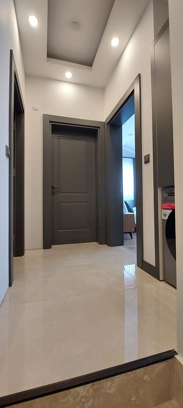 A hallway with a dark door, a trash bin, and a ceiling with recessed lighting. - Professionally Maintained Spacious New Suites 3 (Antalya)