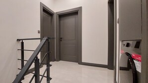 Ein Flur mit einer Metalltreppe, zwei geschlossenen Türen und einem Stromzähler an der Wand.