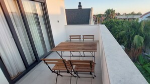 Ein Balkon mit Tisch und Stühlen, umgeben von Grünpflanzen und Blick auf benachbarte Häuser.