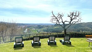 Une terrasse avec quatre chaises et une table, donnant sur une vallée où l’on aperçoit une rivière et des collines.