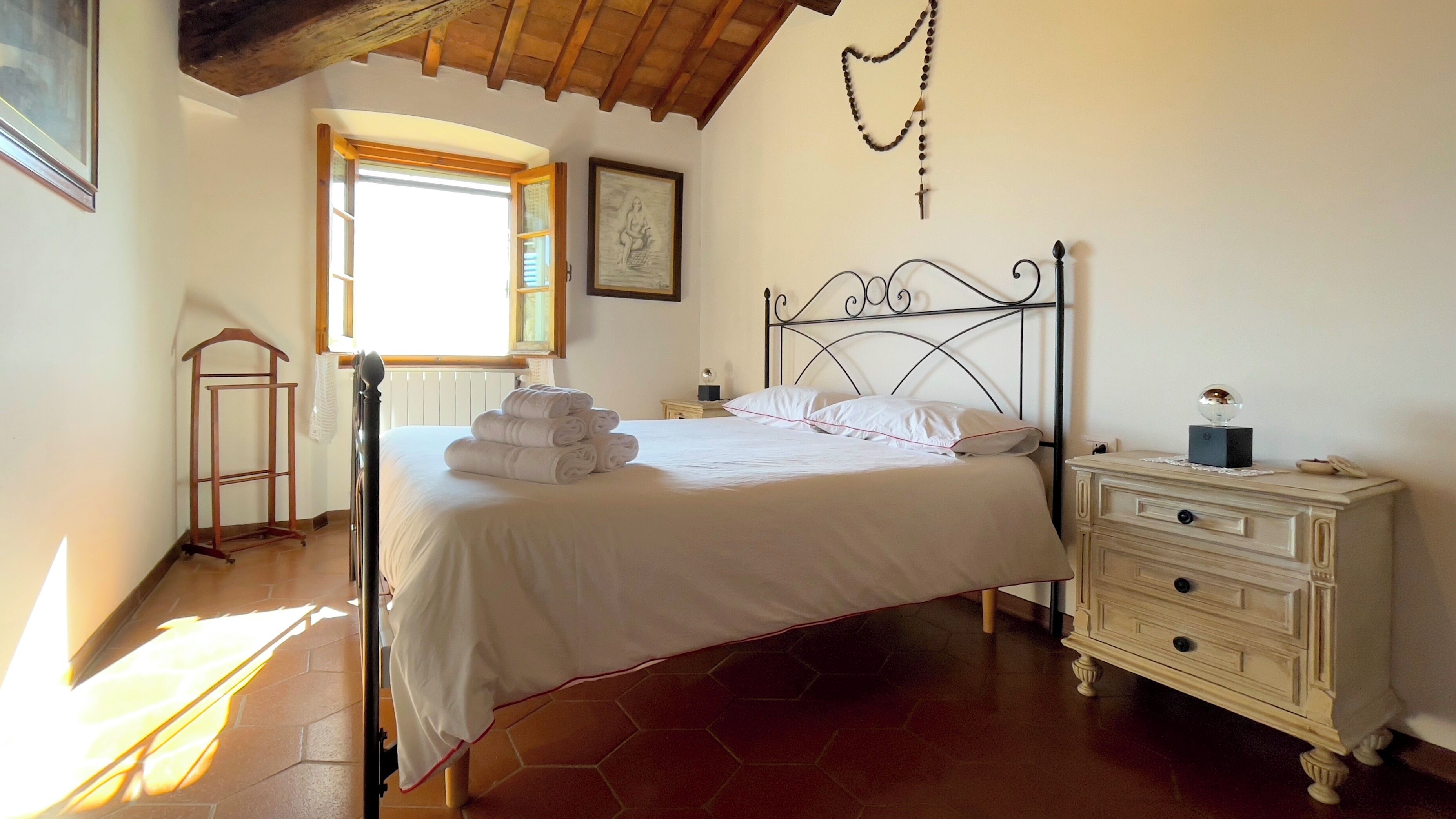 A bedroom with a bed, a nightstand, a dresser, a window, and a painting on the wall.