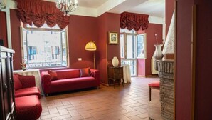A room with a red sofa, a chandelier, a fireplace, and a window with a view of buildings. - Imperial Guest House - Full Apartment no kitchen (Roma)