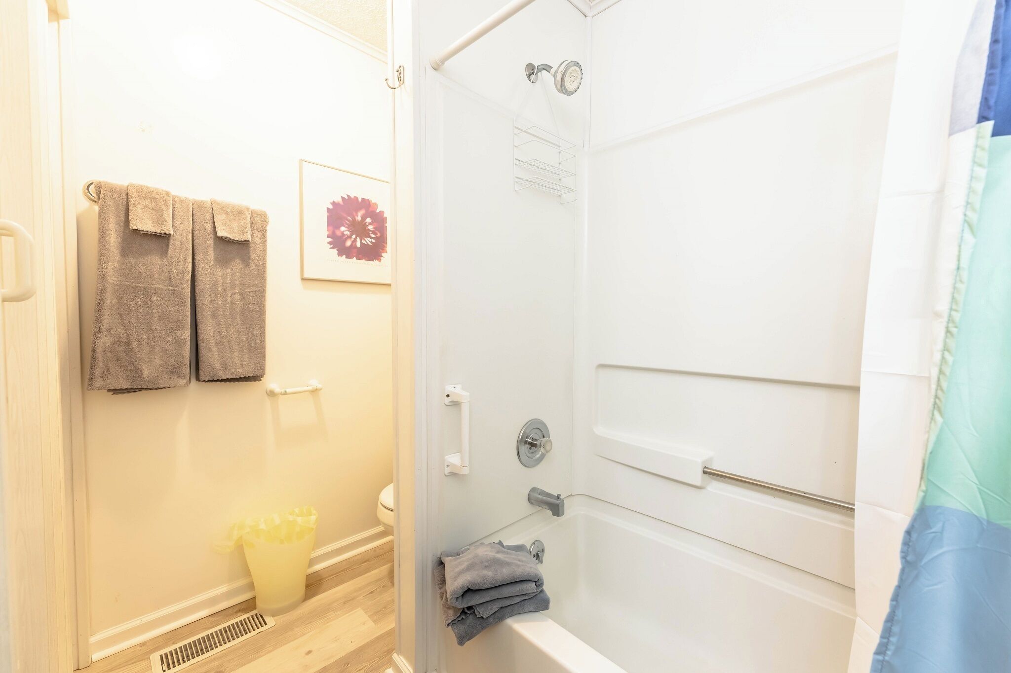 Un bagno con una vasca da bagno, una doccia e un water. Asciugamani appesi al muro e un cestino per la spazzatura a terra.