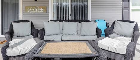 A porch with a wicker sofa and chairs, a metal table, and a welcome sign.