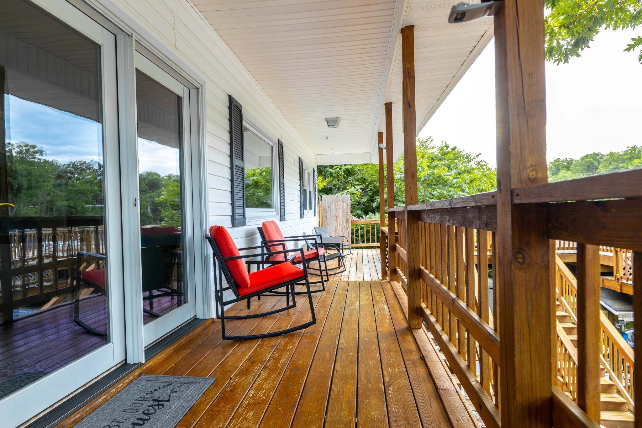 A wooden deck with outdoor furniture, a covered area with sliding glass doors, and a view of greenery.