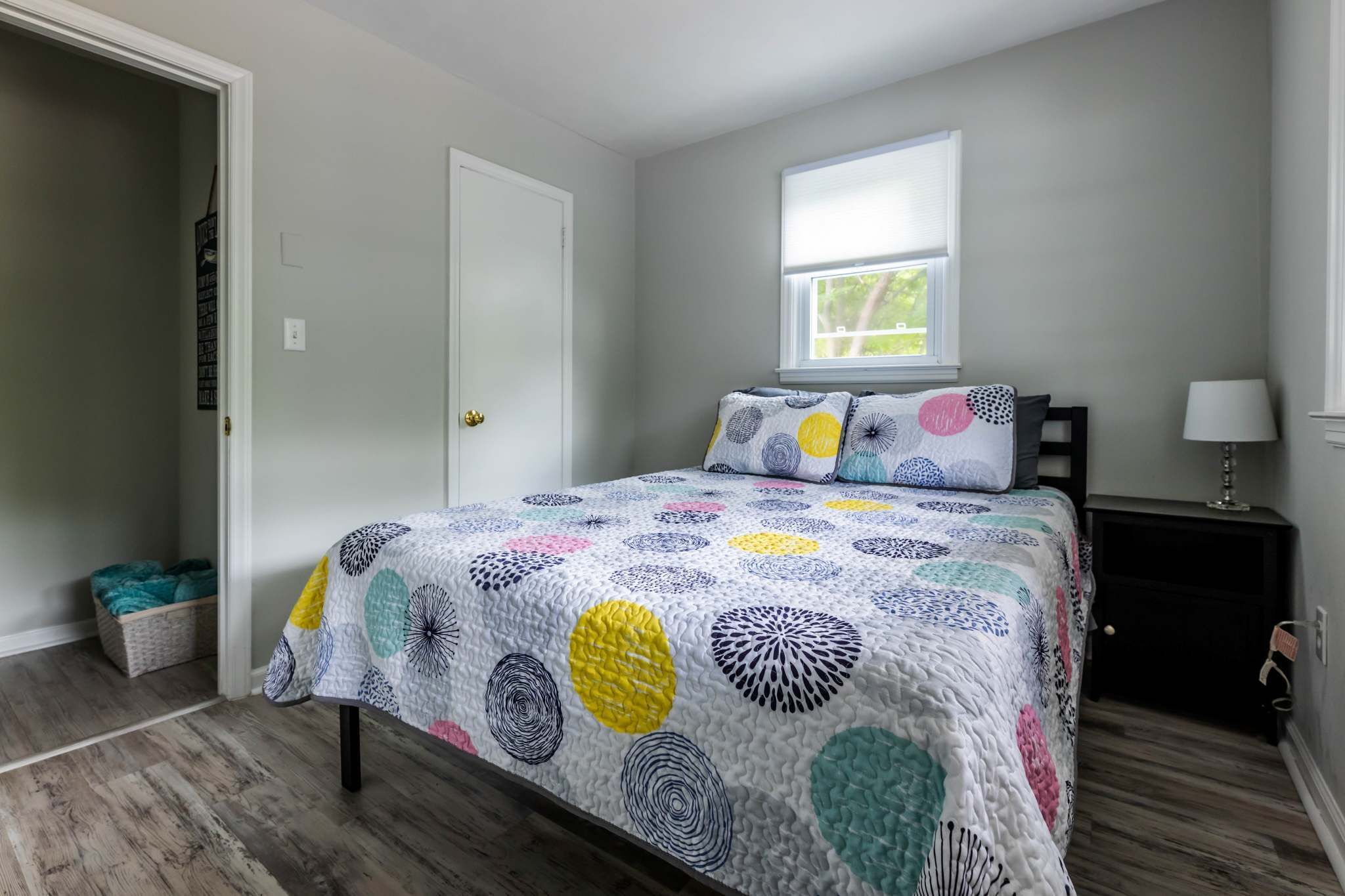 A bedroom with a bed, a window, a nightstand, and a lamp.