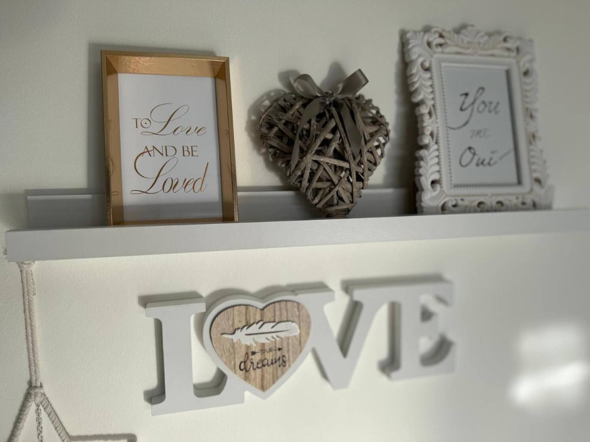 Uno scaffale con oggetti decorativi, tra cui un cartello incorniciato con la scritta “To Love and Be Loved”, un ornamento a forma di cuore e un altro cartello incorniciato con la scritta “You are One”.