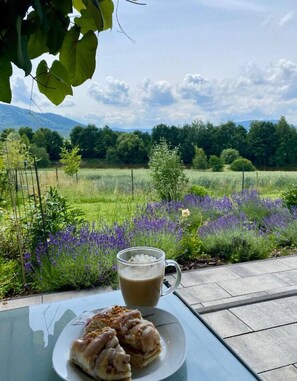 A table with a glass mug and a plate of food, overlooking a field of purple flowers and green trees under a cloudy sky. - Enchanted Hill House of the Beskids (Porabka)