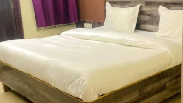 Un lit bien fait, avec du linge de lit blanc, dans une pièce dotée d’une tête de lit en bois et d’un plancher beige.