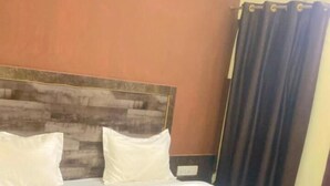 Un lit avec du linge de lit blanc, une tête de lit en bois et un rideau foncé.
